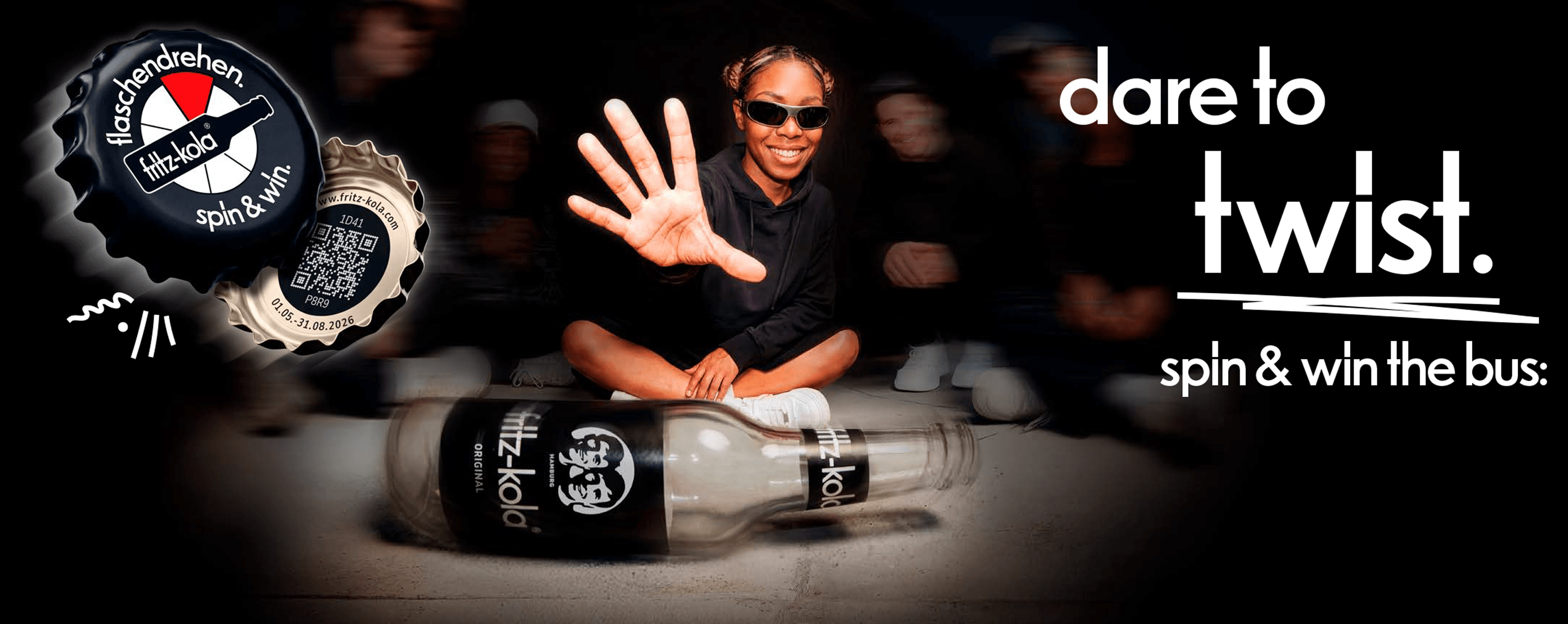 fritz-kola advertising banner: A young woman wearing sunglasses is sitting on the floor, laughing, and holding up a hand with her fingers spread out. Two fritz-kola bottles lie in front of her. On the left is a bottle cap bearing the inscription “flaschendrehen. spin & win” and a QR code. On the right is the slogan “Spin the bottle & win the bus.” alongside an image of a black VW bus in the fritz-kola design.
